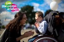 Ein Junge sitzt im Rollstuhl. Vor ihm hockt eine Frau. Beide klatschen in die H&auml;nde.