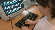 Eine Sch&uuml;lerin sitzt vor einem Bildschirm, der Text stark vergr&ouml;&szlig;ert anzeigt.