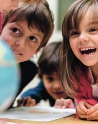 Kinder schauen sich gemeinsam ein Bild auf dem Tisch an, ein M&auml;dchen lacht