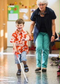 Ein blinder Junge geht Hand in Hand mit einer Frau. In der anderen Hand h&auml;lt er einen Blindenstock.